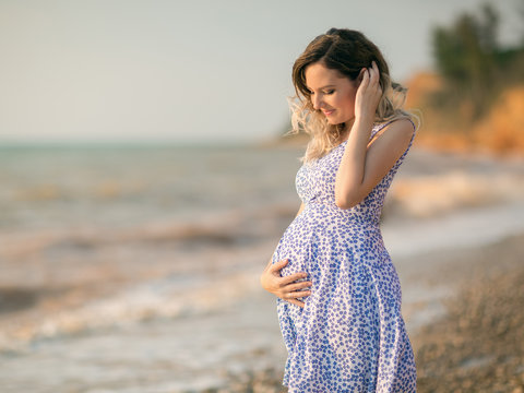 Pretty young pregnant woman posing on the beach by the sea.