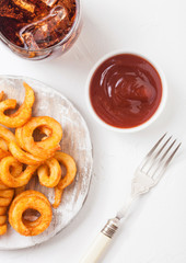 Curly fries fast food snack on wooden board with ketchup and glass of cola on stone kitchen background. Unhealthy junk food
