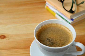 A cup of hot coffee with stack of book and glasses on the wooden table 