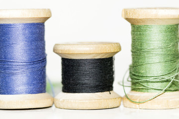 old wooden spools of blue, green and black thread close up