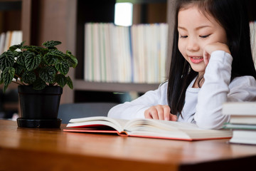 cute girl smiled and standing reading book in the library, children concept, education concept