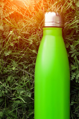 Stainless thermos water bottle, light green color. Mockup isolated on green grass background with sunlight effect. Glossy aluminum vacuum thermo tumbler flask.