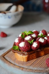 Delicious toast with Ricotta cheese chocolate and raspberries, decorated with mint leaves on vintage cutting board 