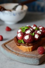 Delicious toast with Ricotta cheese chocolate and raspberries, decorated with mint leaves on vintage cutting board 