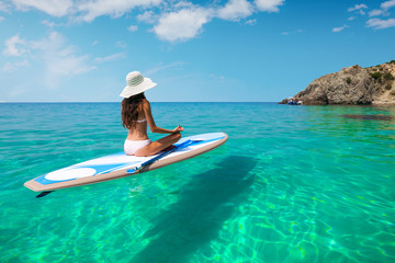 A beautiful young woman relaxes on a SUP board in the sea near the island. Standup paddleboarding on Hawaii.