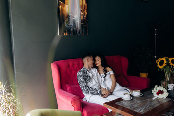 Obraz premium Cheerful newlyweds rest on a bright pink sofa in the cafe