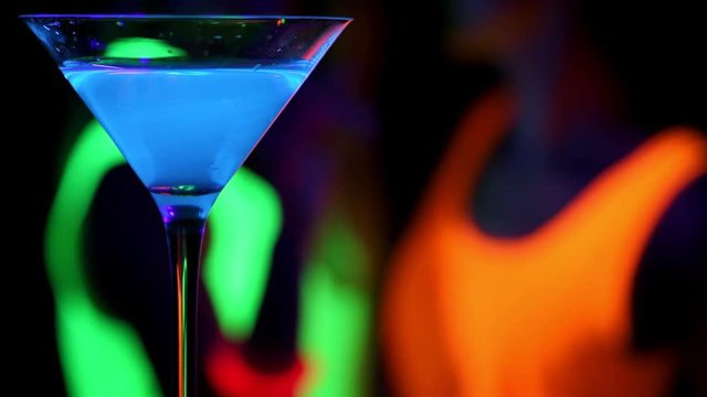 Blue glowing drink with dancing women in UV glow party background. Party concept.