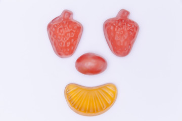 A smiling happy face created with hard and soft sugar candy: strawberry eyes, tangerine mouth. Isolated studio shot.
