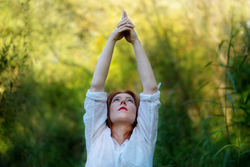 junge rothaarig Frau macht Yoga Übungen mit Hände nach oben in der Natur in Sportkleidung in der Sonne in der Natur