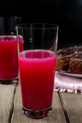 The drink of bright pink color in a transparent glass on the wooden table