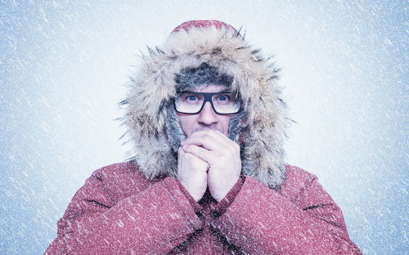 Frozen man in red winter clothes and glasses warming hands, cold, snow, frost, blizzard