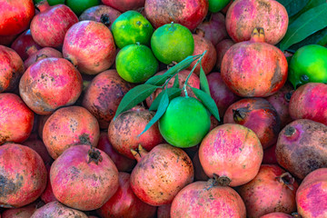 Traditional summer vitamin still life. A lot of ripe pomegranates and a few green mandarins with leaves are laid out on the counter of the Turkish market