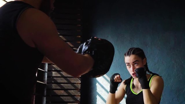 Closeup fit white female boxer training with boxing coach at gym in slow motion. Young slender brunette girl practicing with trainer. Wellness, healthy lifestyle, combat, motivation concept