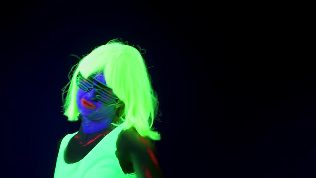 Beautiful sexy woman with UV face paint, wig, glowing glasses, clothing portrait shaking her head. Caucasian woman. Party concept.