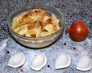 Boiled dumplings with fried bacon and onion lie in a bowl, raw dumplings lie on the table with flour, pepper and onion, Ukrainian national cuisine