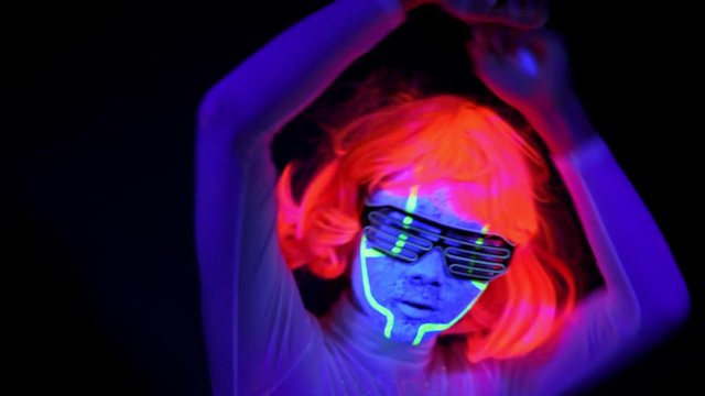 Beautiful sexy woman with UV cyborg face paint, wig, glowing clothing portrait dancing hard, turn around shot. Asian woman. Party concept.