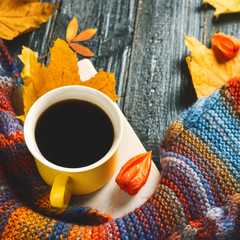 Yellow coffee mug and book on a dark wooden table with autumn scarf and leaves