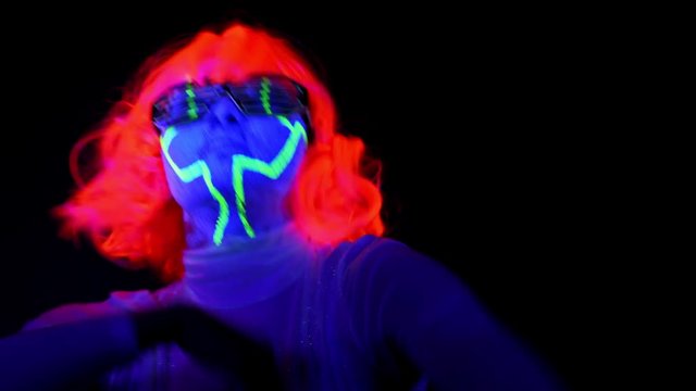 Beautiful sexy woman with UV cyborg face paint, wig, glowing clothing portrait dancing hard. Asian woman. Party concept.