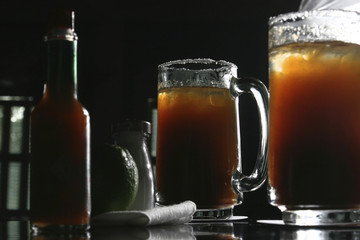 Two michelada jars which are a Mexican beverage made with beer, lime juice, and assorted willows, spices, and peppers. It is served in a chilled, salt-rimmed glass.