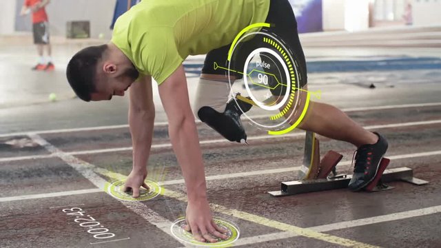 Disabled sportsman with prosthetic leg starting from blocks on indoor stadium track and running; pulse projected in the air and digitally animated countdown appearing on track
