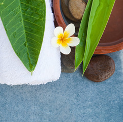 Obraz na płótnie Canvas Top view of flower and two green leaves for spa massage treatment on blue background.