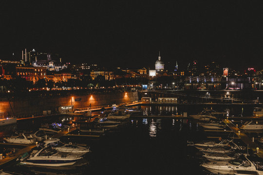 View of illuminated city with boats moored in lake at night