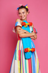 Fashion cool girl posing with a skateboard on pink background.