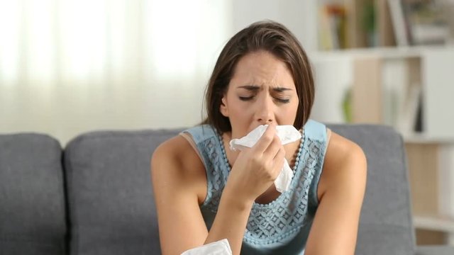 Ill woman blowing mucus and sneezing in a wipe suffering flu symptoms sitting on a sofa at home in winter