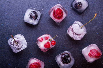 Frozen berries (raspberries, blackberries, blueberries, red currant, cherry) in ice cube over white fabric background.