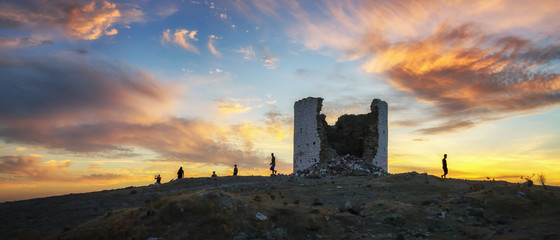 The ruin of a windmill in Bodrum and the silhouettes of people against a coloful sunset sky