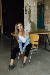 Young blonde woman dressed in casual style sits on a chair