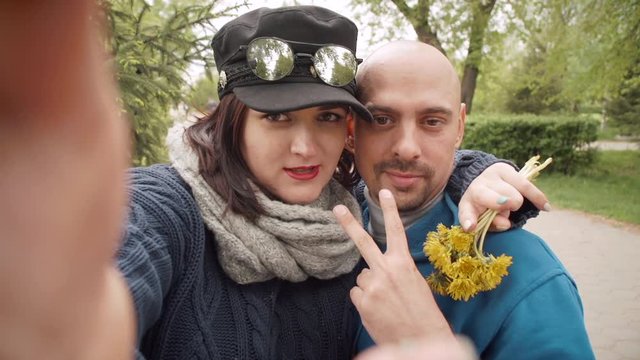 Young happy couple taking a selfie photo using a smartphone in the city park.