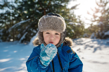Happy cute little boy dressed in warm coverall and hat in winter frozen snowy forest
