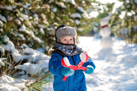 Happy cute little boy dressed in warm coverall and hat in winter frozen snowy forest