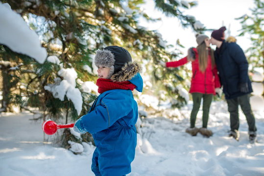 Little boy play with snow and his parents kiss