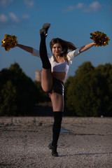 cheerleader girl with pompoms dancing outdoors on sky background