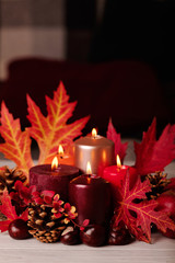 Autumn still life - candles, leaves and cones on the background of pillows.