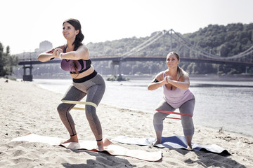Useful activity. Joyful sporty women doing sit ups while exercising on the beach
