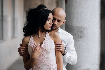 Naklejka premium Handsome young bald headed man hugs with passion young brunette in pink evening dress