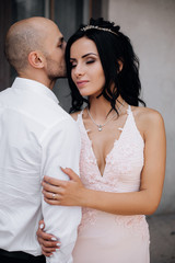 Handsome young bald headed man hugs with passion young brunette in pink evening dress