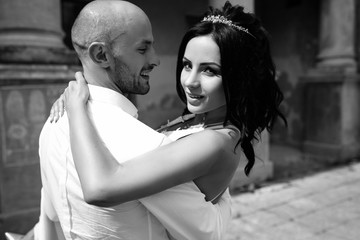 Handsome young bald headed man hugs with passion young brunette in pink evening dress