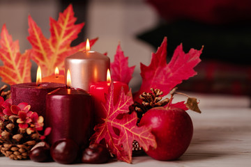 Autumn still life - candles, leaves and cones on the background of pillows.