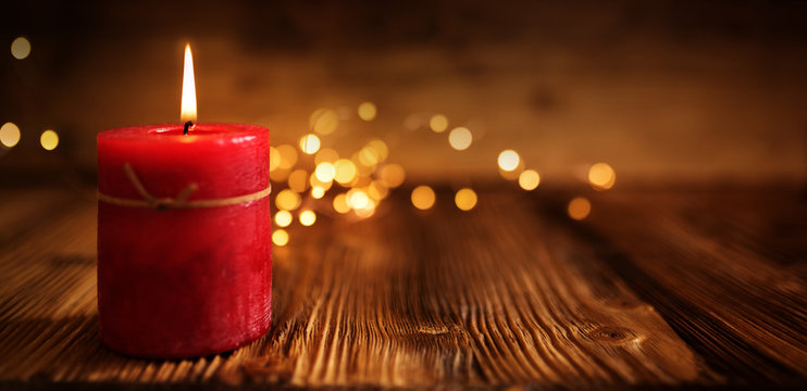 Burning red candle on rustic wood