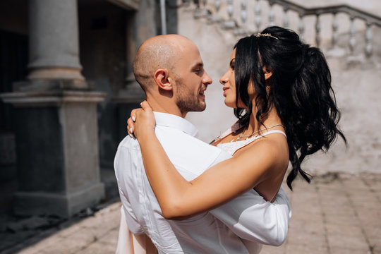 Handsome young bald headed man hugs with passion young brunette in pink evening dress
