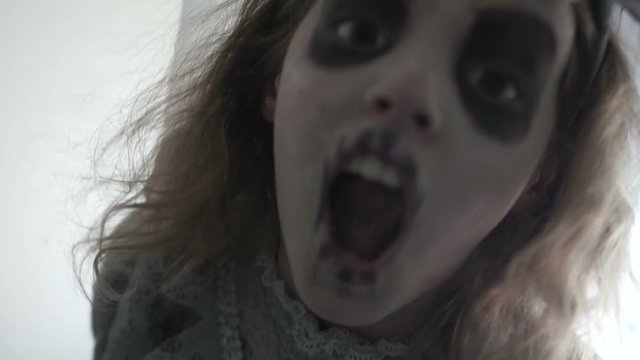 A child dressed as a dead bride screams bending over the camera. Gray Halloween, All Saints Day