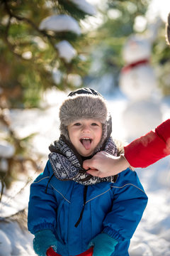 Happy cute little boy dressed in warm coverall and hat in winter frozen snowy forest. Mother care