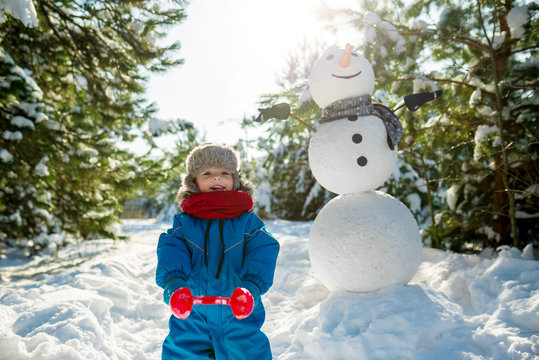 Little boy plays in snow and makes snowballs near large snowman