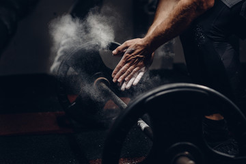 Weightlifter preparing for training workout lifter barbell. Hands in dust and talc. Dark background.