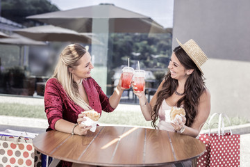 Tasty lunch. Cheerful happy women smiling to each other while raising glasses with lemonade
