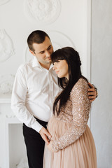 Man hugs pregnant woman tender standing in a bright room